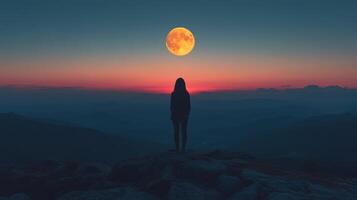 Woman standing on a mountain peak under a full moon at dusk with vibrant sky colors photo