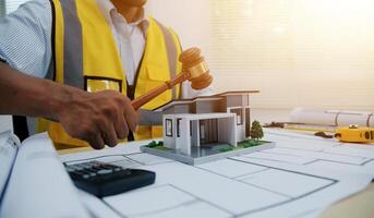 Judge gavel on building blueprint plans with a yellow safety helmet in the background. law that deals with matters relating to building construction, engineering. Construction law concept. photo