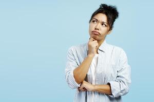 Pensive young woman reflecting with hand on chin on blue background photo