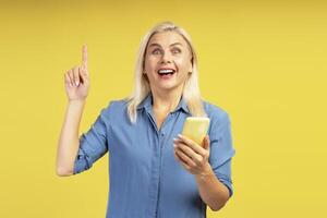 Excited woman having an idea while using smartphone on yellow background photo