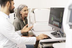 Ophthalmologist explaining diagnosis to senior patient using computer in clinic photo