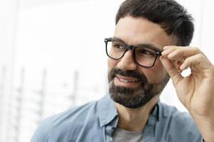 Handsome bearded man trying new eyeglasses in optical store photo
