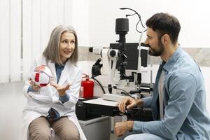 Senior female doctor explaining eye anatomy to patient using model in ophthalmology clinic photo