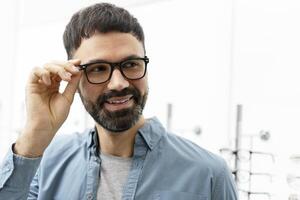 Handsome bearded man trying eyeglasses in optical store photo
