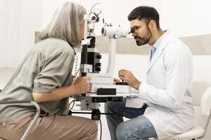 Senior woman undergoing eye exam with optometrist using slit lamp photo