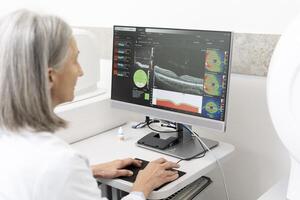 Senior doctor analyzing optical coherence tomography scan on computer in ophthalmology clinic photo