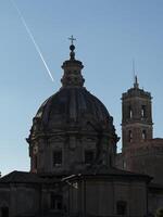 Historic dome and bell tower under a clear sky with contrails contrasting the ancient architecture at sunset in a European city photo