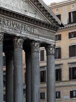Historic columns of ancient temple stand resilient against a backdrop of elegant Roman architecture during daylight in Rome photo