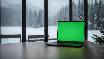 Laptop with Green Screen on a Table by a Window with a Snowy Mountain View photo