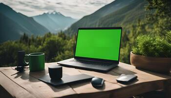 Laptop with Green Screen on Wooden Table with Mountain View photo
