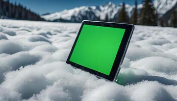 Tablet in the snow with a green screen, snowy mountains in the background photo