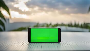 Smartphone with Green Screen on a Table with Blurred Sunset Background photo