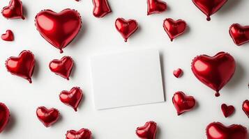 Bright red heart-shaped balloons are scattered around a blank card on a white surface, creating a playful atmosphere perfect for love notes or celebratory messages, ideal for any romantic occasion. photo