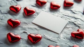 Red hearts scattered around a blank card create a romantic atmosphere on a textured surface. Perfect for personal messages or expressions of love, this arrangement evokes warmth and affection. photo