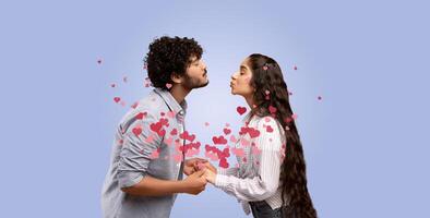 Indian couple stands facing each other, sharing an affectionate kiss. Surrounded by floating hearts, they hold hands in a moment of love and connection during a special celebration. photo