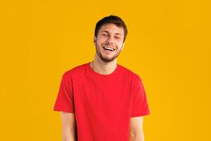 Portrait of handsome guy smiling and looking at camera over blue studio background. Happy caucasian man with shy facial expression posing, male student model showing positive emotions and laughing photo