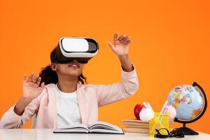 New Experience In Education And Knowledge. Black teenager using modern VR glasses for studying, gesturing on orange yellow studio background, sitting at desk with globe and books, free copy space photo