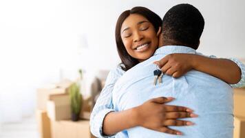 House ownership concept. Excited black woman holding house key and hugging her husband, being happy over moving to new apartment with her boyfriend, free space photo
