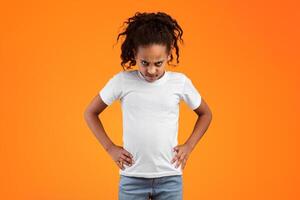 Grumpy Person. Serious furious black girl standing and putting hands on hips, posing over orange studio background, feeling angry and displeased, having bad mood, looking at camera and frowning photo
