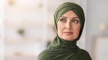 Headshot Of Mature Muslim Female Wearing Green Hijab Posing Looking Aside Standing Indoors. Panoramic Shot, Portrait Of Beautiful Senior Middle-Eastern Lady Concept. Free Space For Text photo