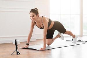 Smiling Lady Training At Home In Front Of Cellphone On Tripod, Beautiful Female Fitness Blogger Shooting Tutorials, Doing Cross Body Mountain Climbers Exercise At Camera Having Call With Trainer photo