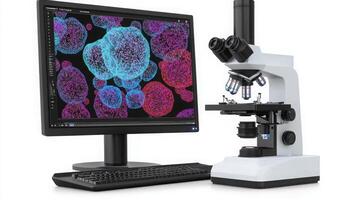 A microscope is positioned next to a computer displaying colorful biological cell imagery. photo