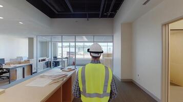 A construction management expert stands in a newly developed office, equipped with a hard hat and safety vest. He interacts with AI tools while surveying the workspace and planning for completion. photo
