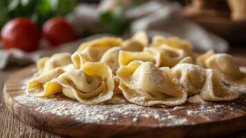 Freshly made pasta is arranged on a wooden cutting board, dusted with flour. The setting features rustic kitchen elements and a few tomatoes in the background, creating a warm culinary atmosphere. photo