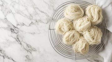 Homemade pasta is artistically arranged in nests on a wire rack, ready to dry. The marble countertop adds elegance to the cozy kitchen setting. photo