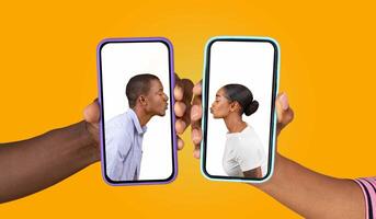 Two individuals hold smartphones, each displaying the other face as they share a playful kiss gesture. The bright yellow background enhances the warm, loving atmosphere of their connection. photo