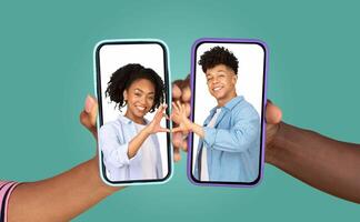 A couple smiles while using their smartphones to chat and express affection. Their hands create a heart shape on the screens, showcasing modern communication and romance. photo