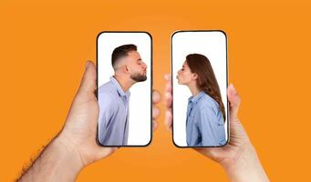 Two hands hold smartphones displaying a couple playfully kissing through chat. The bright orange background highlights their connection and affection in a modern digital setting. photo