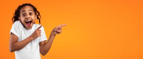 Great Offer Concept. Portrait Of Excited Black Girl Pointing Two Fingers Aside At Free Copy Blank Space For Text Standing On Yellow Orange Studio Background. Look There, Panorama, Banner photo