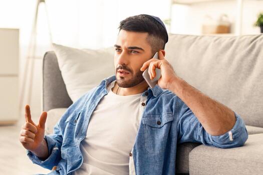 corporativo negocio comunicación concepto. retrato de enfocado joven judío chico haciendo teléfono llamar, trabajando en computadora, sentado en piso y propensión en sofá en vivo habitación, que se discute proyecto plan foto