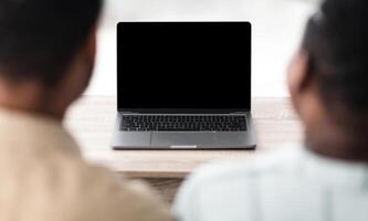 Rear View Of Black Couple At Laptop Having Call Sitting Near Computer With Blank Screen Communicating Online Indoor. Modern Remote Communication Concept. Selective Focus, Mockup photo