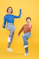 A mother and her daughter dance joyfully against a bright yellow background. They express happiness and affection, showcasing their strong bond through fun and playful movement. photo