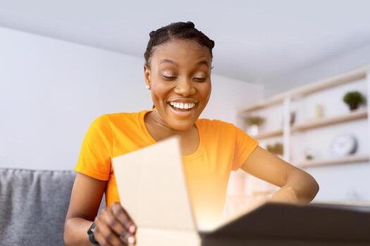 entrega, remoto compras concepto. sonriente negro mujer desembalaje cartulina paquete, contento con su compra a hogar. satisfecho hembra cliente recepción su orden desde en línea Tienda foto