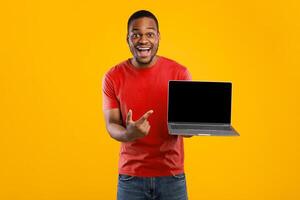 Great Website. Excited African American Man Showing Laptop Computer Blank Screen To Camera Posing Over Yellow Studio Background. People And Gadgets, Technology Concept. Mockup photo