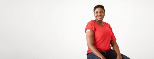 Cheerful African Woman Showing Vaccinated Arm After Coronavirus Antiviral Injection Posing Sitting On White Background, Smiling To Camera. Covid-19 Vaccination Banner. Panorama, Empty Space For Text photo