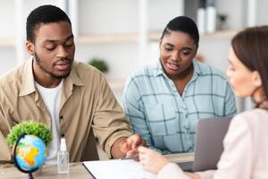 African American Tourists Couple Signing Papers During Consultation With Female Travel Agent Purchasing Vacation Tour Sitting In Modern Office Indoors. Selective Focus photo