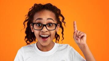 Wow, Eureka. Heashot portrait of emotional black student girl having great idea, finding inspiration or solution to problem. Excited pupil in glasses with open mouth pointing finger up, studio wall photo