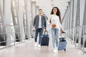 Ready For Journey. Happy Arab Man And Woman Walking With Luggage In Airport, Smiling Young Middle Eastern Travellers Carrying Suitcases While Going To Departure Gate In Terminal, Copy Space photo