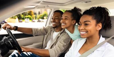 Happy Black Parents And Daughter Riding A Car Smiling Looking Aside Sitting In Seats Enjoying Road Trip By Auto. Automobile Tourism, Traffic And Transportation Concept. Side View, Selective Focus photo
