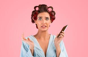Oops. Embarassed Housewife Holding Mobile Phone Looking At Camera In Confusion Posing On Yellow Studio Background. photo