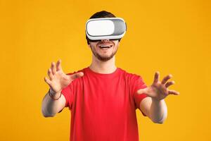 Cyberspace And Futuristic Technology Concept. Smiling guy wearing VR headset touching air during virtual reality experience. Happy bearded man exploring artificial computer world, blue studio wall photo