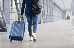 Rear View Of Unrecognizable Man Walking With Suitcase In Airport Terminal, Male Traveller Going To Flight Boarding Gate, Ready For Vacation Journey Or Business Trip, Cropped Image, Copy Space photo