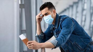 Missed Flight. Frustrated Middle Eastern Man In Medical Mask Looking At Passport And Tickets While Standing In Airport Terminal, Depressed Arab Guy Suffering Problems While Travelling During Pandemic photo