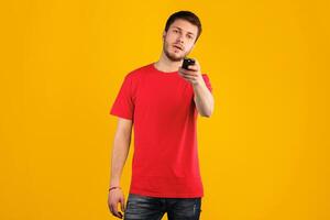 Watching Tv. Portrait of bearded caucasian guy holding remote control in hand, switching channels and programs, standing at studio, isolated over blue background wall. Spending Time At Home photo