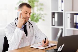 High Quality Service Concept. Portrait of confident male therapist talking on smartphone and writing in his notebook, taking notes about appointment, consulting client. Remote Communication photo