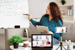 Remote Lecture. Young lady teacher explaining math formulas, giving online lesson, sitting at desk, filming vlog. Woman recording blog for her internet channel and making live videochat photo